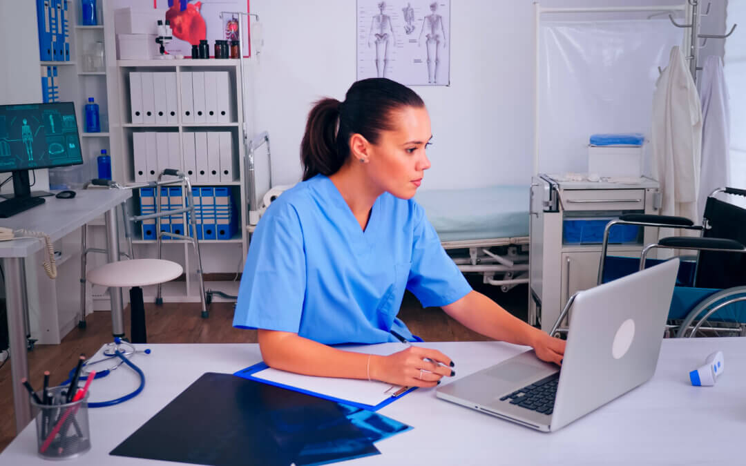Infirmière en tenue professionnelle travaillant sur ordinateur dans un bureau de soin